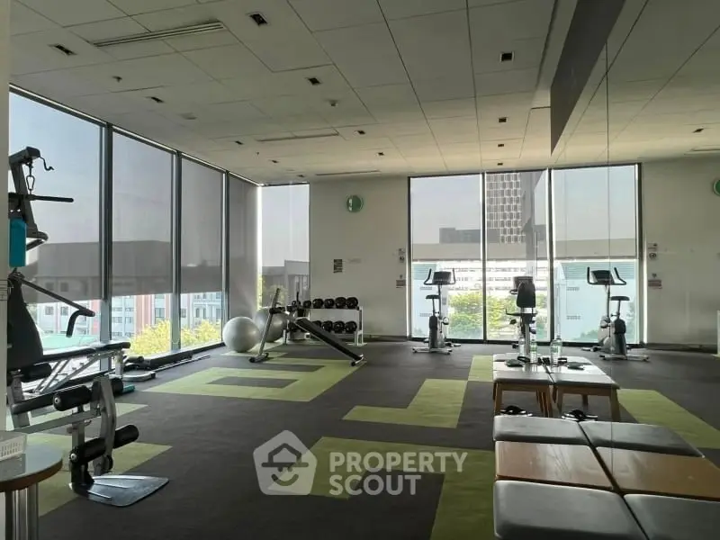 Spacious gym with modern equipment and large windows offering city views.
