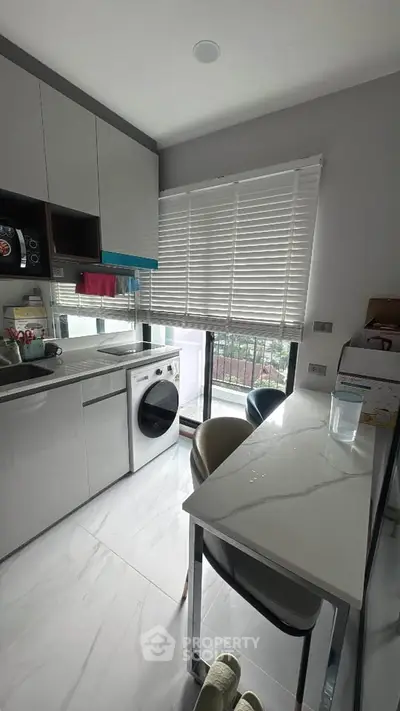 Modern kitchen with sleek appliances and dining area, featuring a washing machine and large window view.