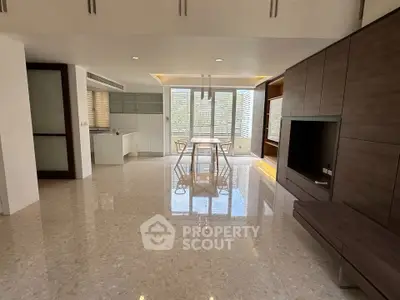 Spacious modern living room with open kitchen and dining area, featuring sleek cabinetry and large windows.