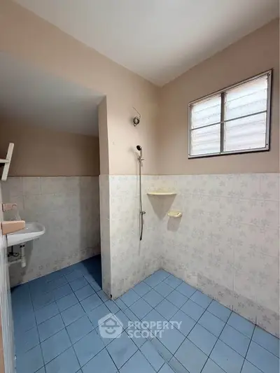 Spacious bathroom with blue tiled floor and shower area, featuring a window for natural light.