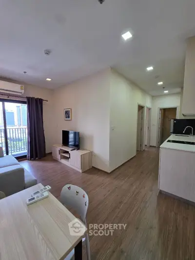 Modern open-plan living room with kitchen, featuring wooden flooring and balcony access.