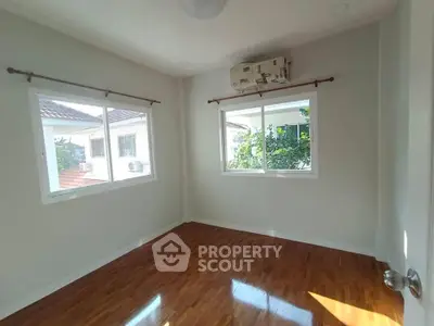 Bright empty room with wooden flooring and large windows in a modern home.