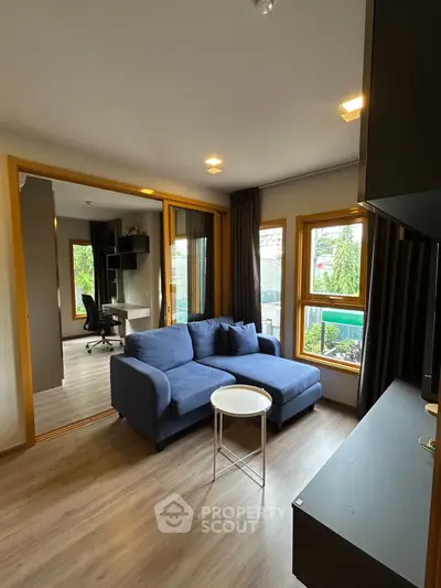 Modern living room with blue sofa, large windows, and wooden flooring in a stylish apartment.