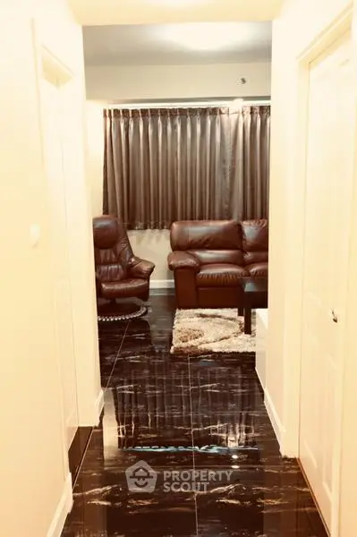 Elegant hallway leading to a cozy living room with leather seating and glossy marble flooring.