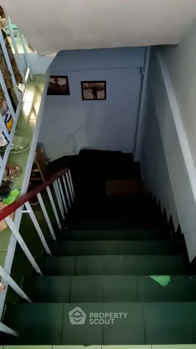 Staircase in a residential building with green steps and white railings, leading to a lower floor.