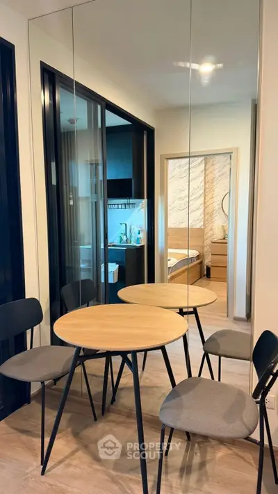 Modern dining area with round table and chairs, mirrored wall reflecting stylish interior design.