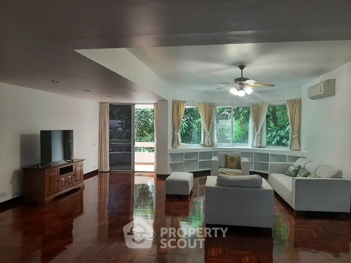 Spacious living room with polished wooden floors, large windows, and modern furniture.