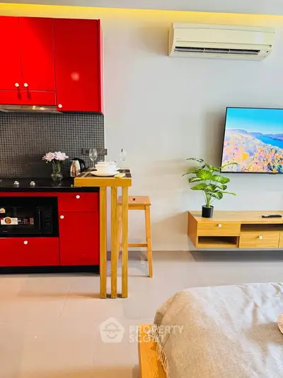 Modern kitchen and living area with red cabinets and wall-mounted TV
