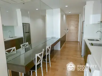 Modern kitchen with sleek design, glass dining table, and wooden flooring in a stylish apartment.