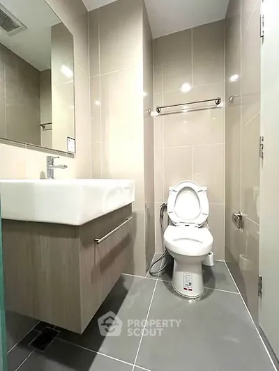 Modern bathroom with sleek fixtures and neutral tiles, featuring a contemporary sink and toilet.