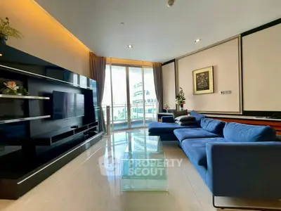 Luxurious living room with modern blue sofa and glass coffee table, featuring a large TV and balcony view.