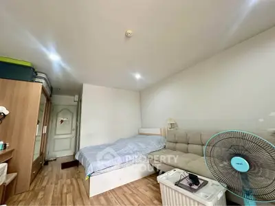 Cozy bedroom with wooden flooring, bed, sofa, and fan, ideal for comfortable living.