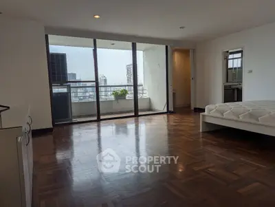 Spacious bedroom with parquet flooring and balcony view in urban apartment