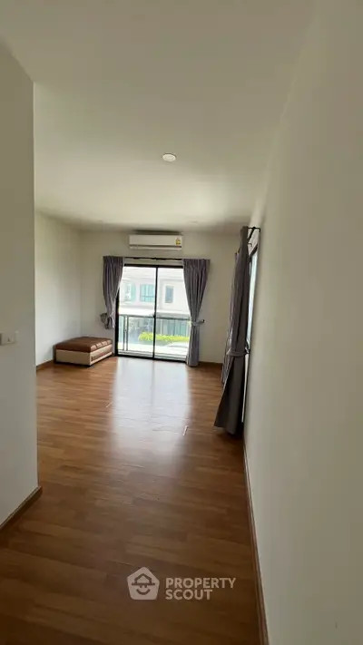 Spacious empty room with wooden flooring and large windows for natural light.