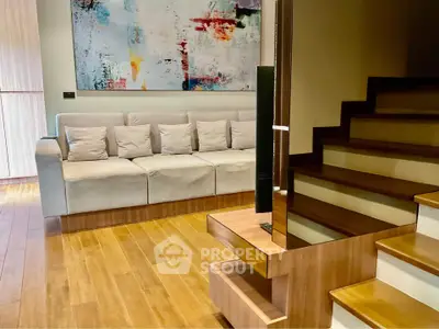 Modern living room with stylish staircase and abstract art, featuring a cozy sofa and wooden flooring.