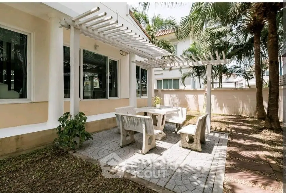 Charming outdoor patio with pergola and stone seating in lush garden setting.