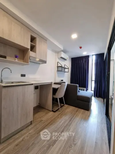 Modern studio apartment with sleek kitchen and cozy living area, featuring wood flooring and ample natural light.