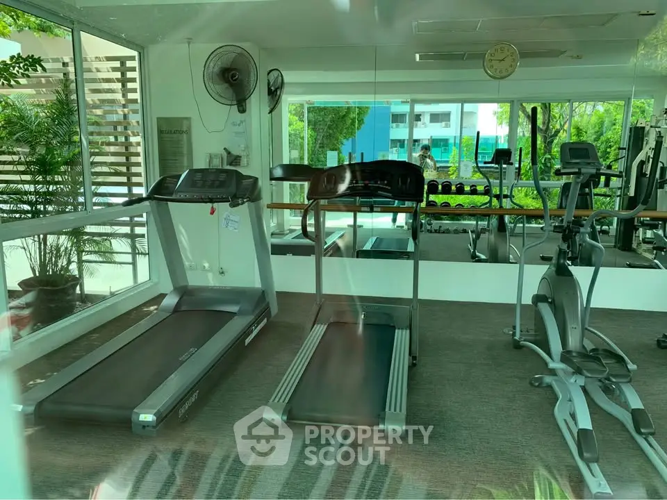 Modern gym with treadmills and exercise equipment in a bright, spacious room with large windows.