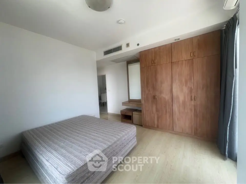 Spacious bedroom with wooden wardrobe and large window for natural light.