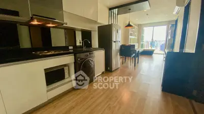 Modern open-layout kitchen with sleek appliances and dining area, featuring a washing machine and large windows.