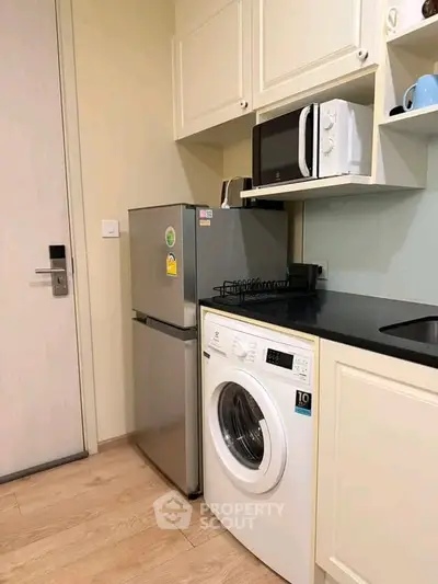 Compact kitchen with modern appliances including fridge, microwave, and washing machine in cozy apartment.