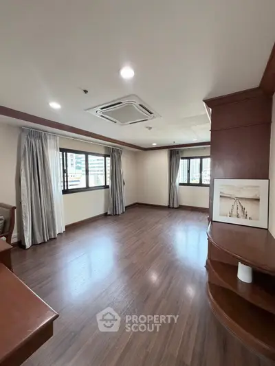 Spacious empty living room with wooden floors and large windows in modern apartment.