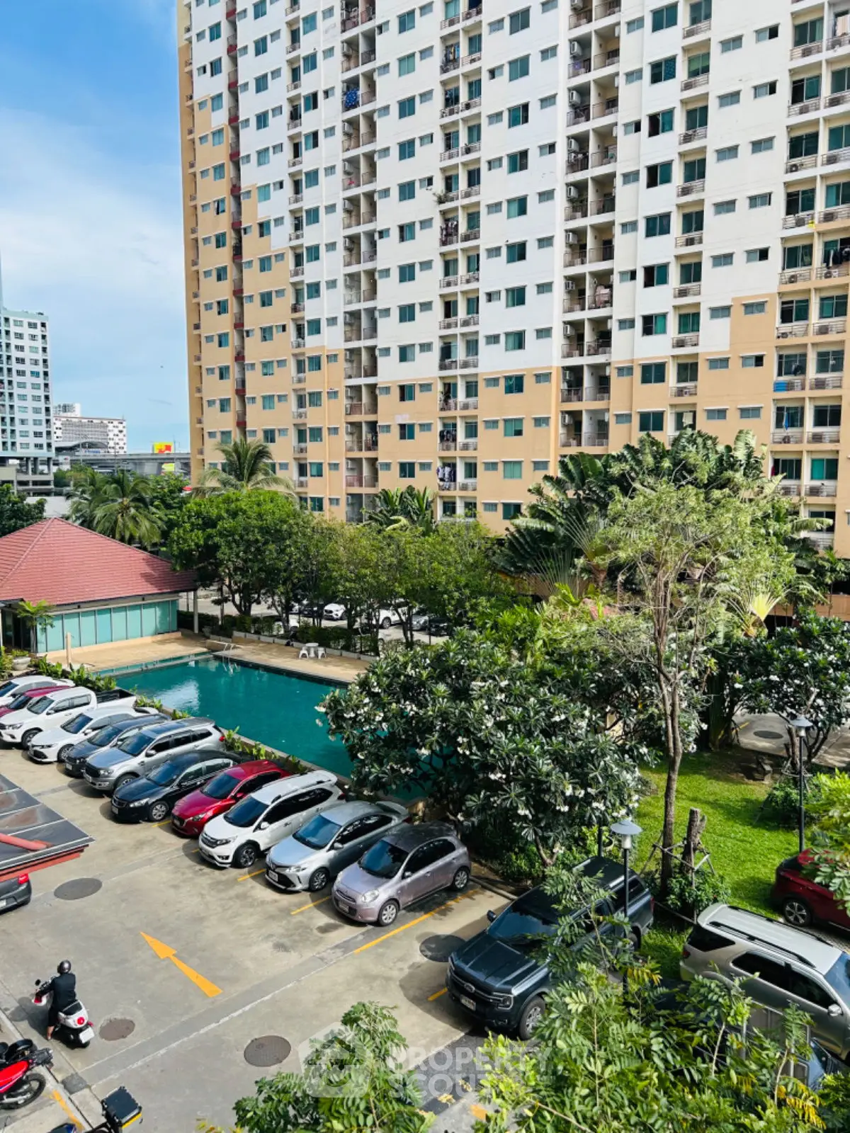 High-rise residential building with pool and parking area in lush green surroundings.