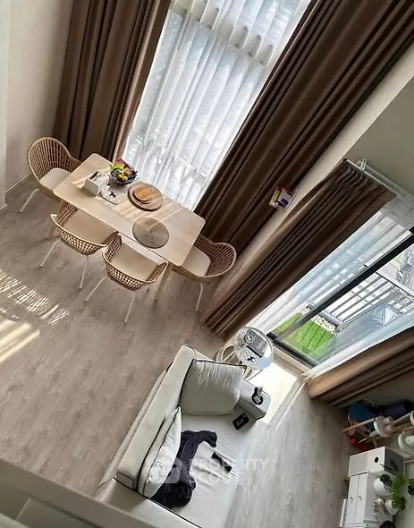 Modern living room with high ceiling and large windows, featuring cozy seating and dining area.