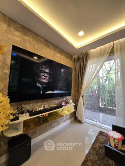 Stylish living room with large TV and elegant decor, featuring floor-to-ceiling windows and lush garden view.