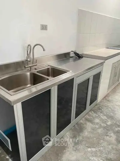 Modern kitchen with stainless steel sink and countertop, sleek cabinetry, and tiled backsplash.