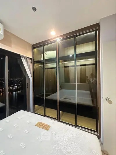 Modern bedroom with large mirrored wardrobe and city view from window.