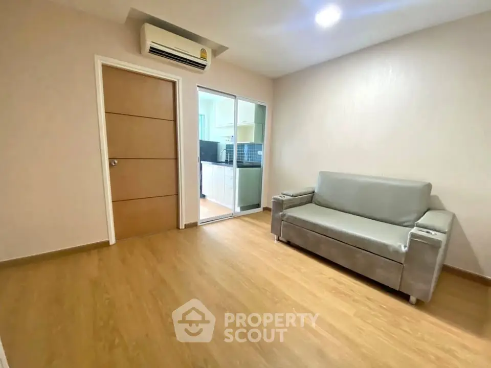 Modern living room with sleek sofa and wooden flooring, adjacent to a stylish kitchen.