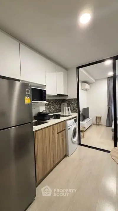 Modern kitchen with stainless steel appliances and open layout leading to living area.