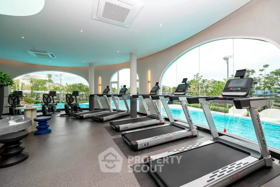 Luxurious gym with modern equipment and pool view in upscale residential complex.
