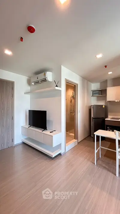 Modern open-plan living room with kitchen and TV, featuring sleek design and natural light.