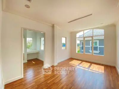 Spacious sunlit room with wooden flooring and large windows offering a serene view.