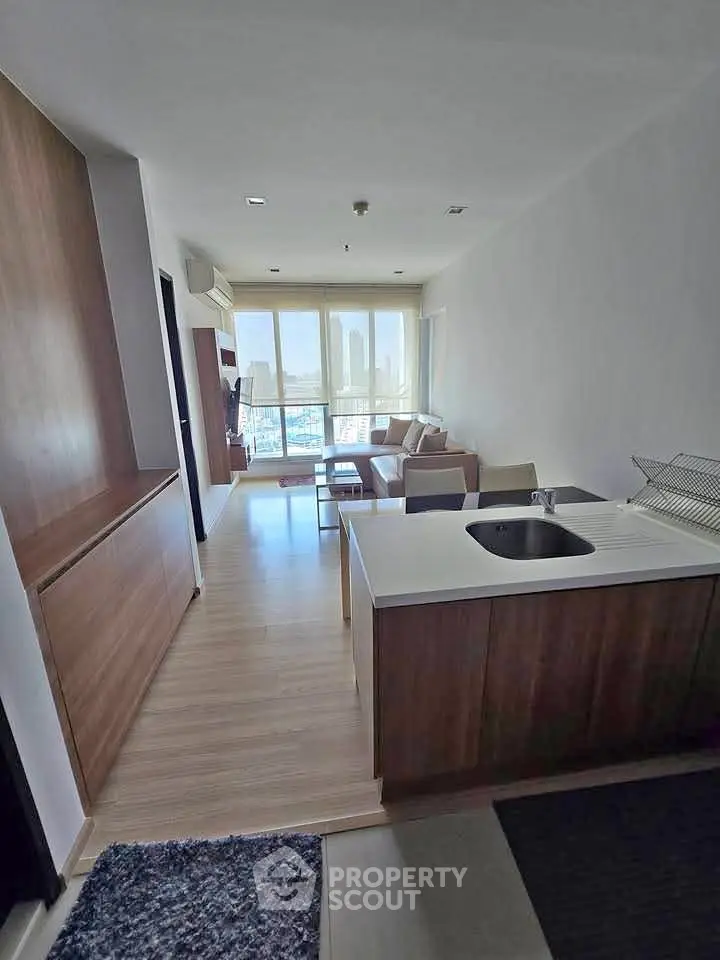 Modern open-layout living room with kitchen island and city view, featuring sleek wooden finishes and ample natural light.