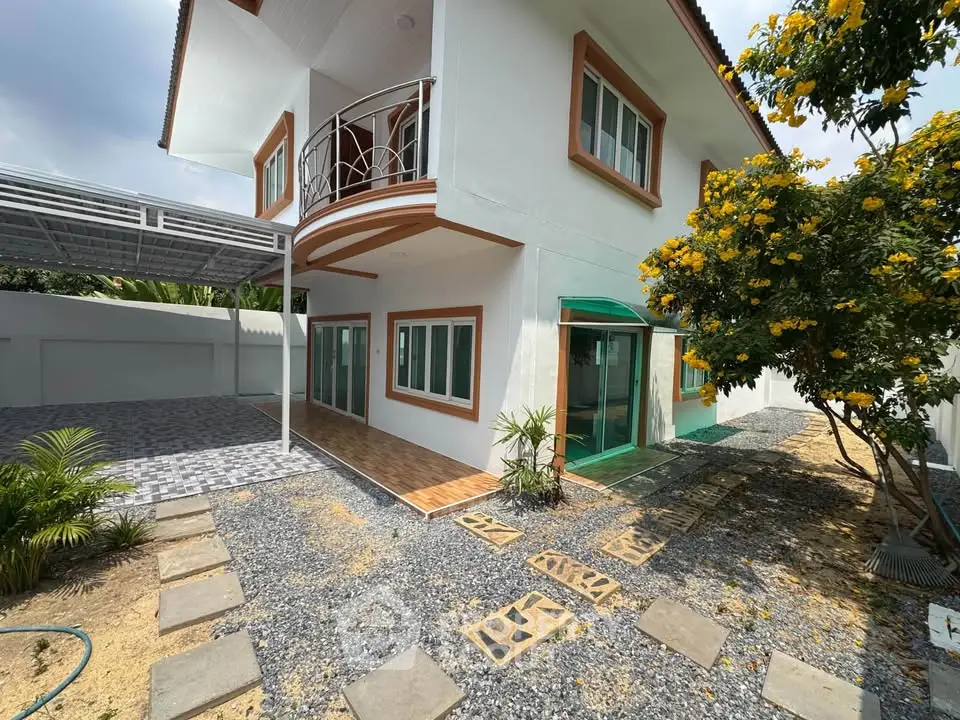 Charming two-story house with balcony and landscaped garden, featuring a covered carport and modern exterior design.
