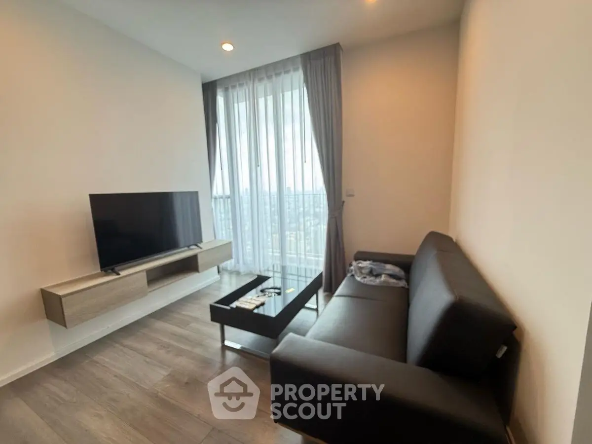 Modern living room with sleek furniture and large window offering city views.