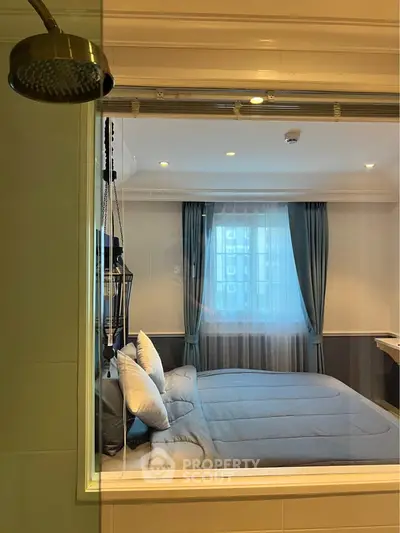 Modern bedroom with large window and adjacent shower area, featuring elegant decor and soft lighting.