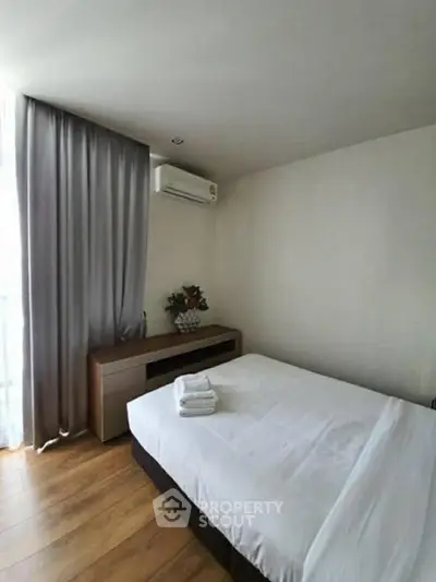 Cozy bedroom with wooden flooring and natural light, featuring a neatly made bed and air conditioning.