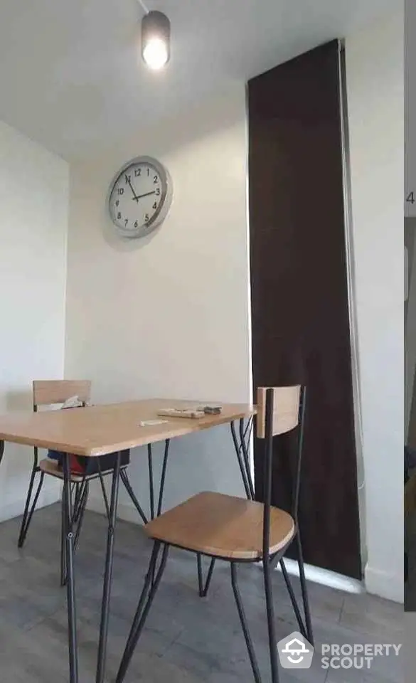 Modern dining area with minimalist table and chairs, featuring a wall clock and sleek flooring.