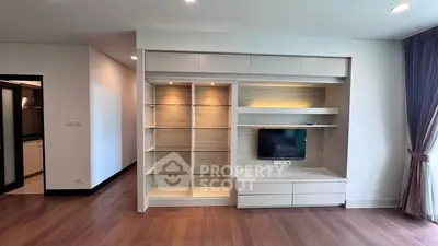 Spacious living room with modern built-in shelving and TV, featuring elegant wooden flooring and natural light.