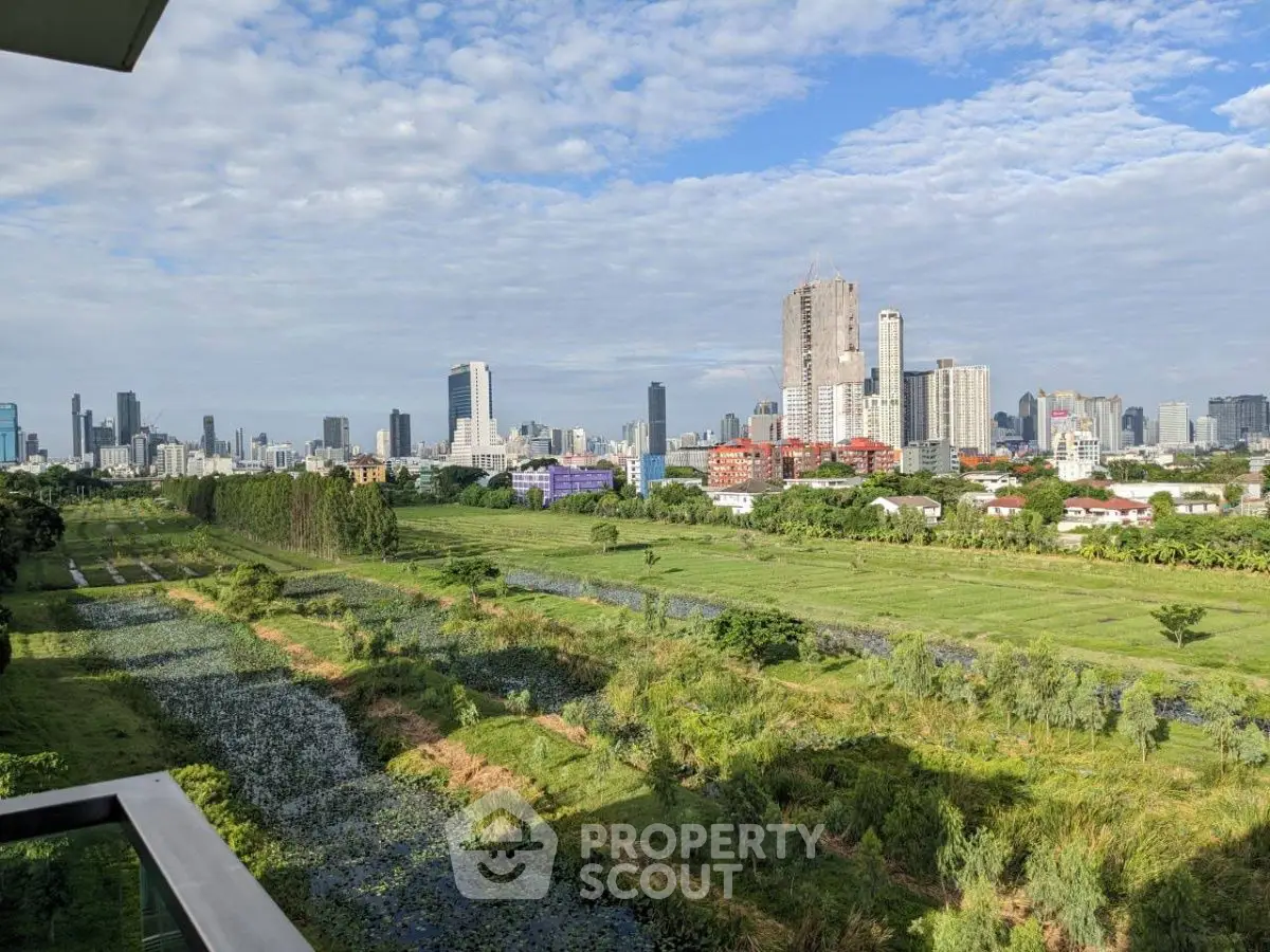 Stunning cityscape view from a balcony overlooking lush green fields and urban skyline.