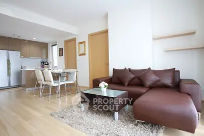 Modern open-plan living room with brown leather sofa and sleek kitchen area.