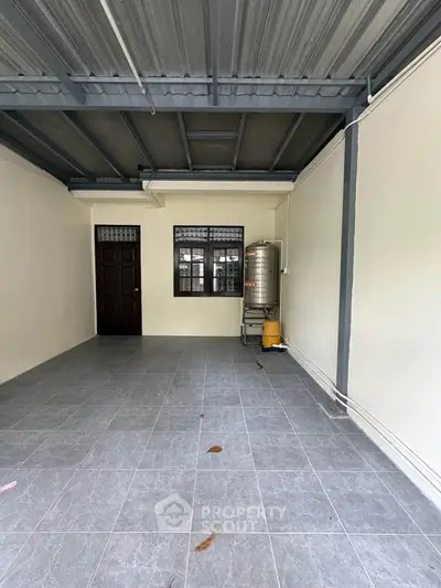 Spacious tiled area with metal roof and water tank, ideal for storage or parking.
