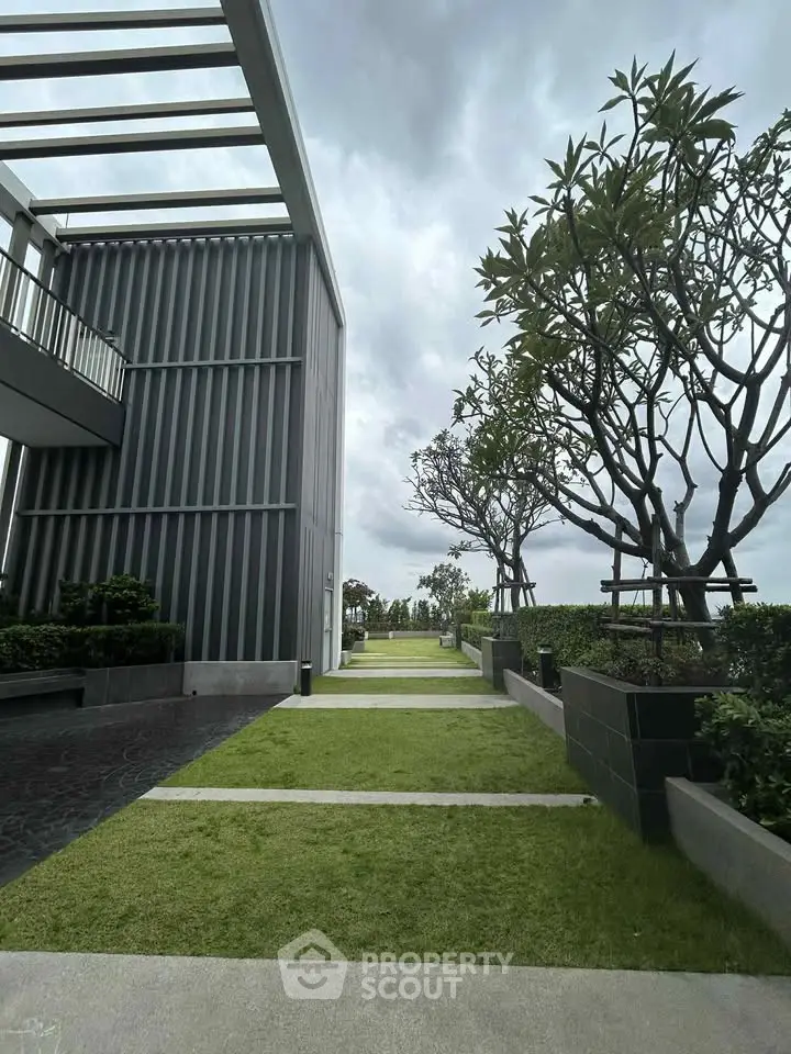 Modern building exterior with landscaped garden and pathway under cloudy sky.