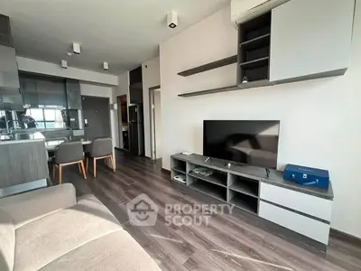 Modern living room with sleek furniture and open kitchen layout, featuring a large TV and stylish shelving.