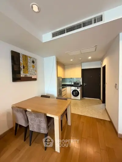 Modern dining area with wooden flooring and compact kitchen featuring washing machine.