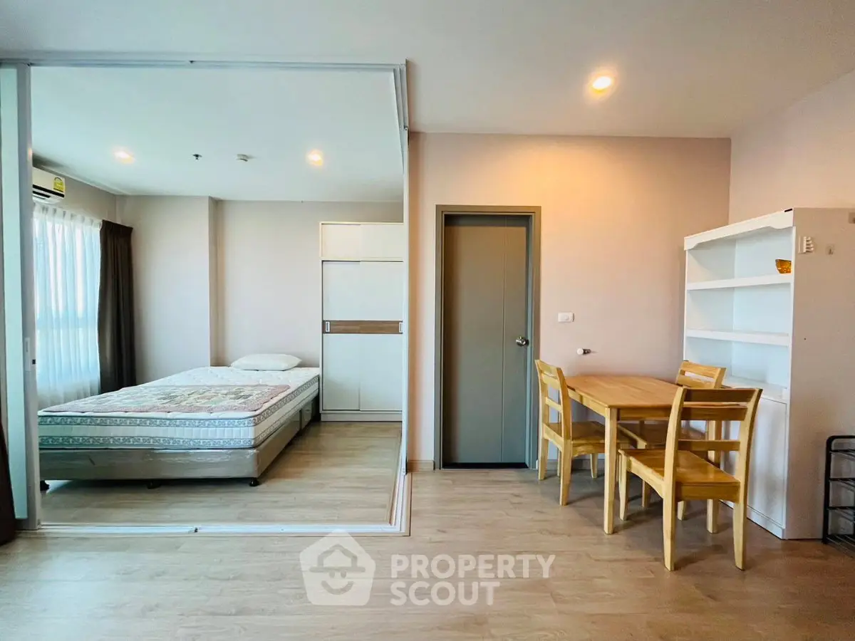 Modern studio apartment with cozy bedroom and dining area, featuring wooden flooring and ample natural light.